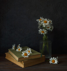 Daisies, books, decanter on a dark background