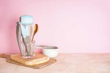 Kitchen utensils in a glass on a pink background with place for text.