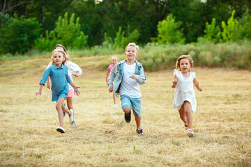 Fototapeta premium Kids, children running on meadow in summer's sunlight. Look happy, cheerful with sincere bright emotions. Cute caucasian boys and girls. Concept of childhood, happiness, movement, family and summer.