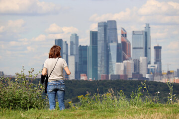 Woman standing on top of a hill on a Moscow city background. Summer travel and leisure, urban landscape with skyscrapers