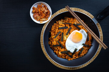 Homemade Kimchi Fried rice topped with fried egg on skillet, overhead view on black wooden table.