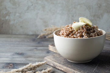 Buckwheat porridge in the beige bowl with piece of butter on the vintage wooden pan with wooden spoon
