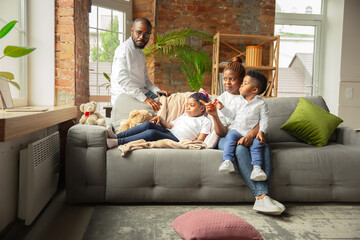 Obraz premium Young and cheerful african family during quarantine, insulation spending time together at home. Time for family, happiness and love. Concept of quarantine lifestyle, togetherness, home comfort.