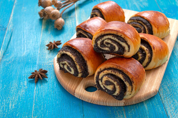 Obraz na płótnie Canvas Tasty buns rolls with poppy filling on a blue wooden background.