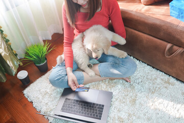 Asian woman and her puppy holding credit card and using laptop computer online shopping at home....