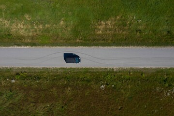 Top drone view of black car on asphalt road in countryside. Tire tracks.