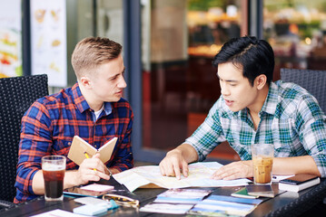 Multi-ethnic friends planning summer vacation, checking map and writing down notes