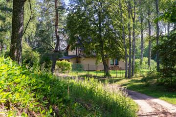 Countryside road between green grass and trees. Private house near the forest. Modern exterior.