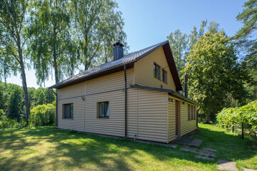 Fototapeta na wymiar Countryside private house near the green forest. Modern exterior of cottage. Siding walls with windows. Tiled roof with chimney pipe.
