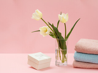 Bouquet of yellow tulips in vase with towels on a pink background.