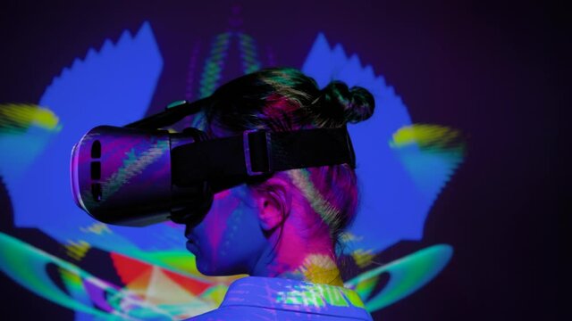 Woman using virtual reality headset, looking around at interactive technology exhibition with changing multicolor projector light illumination. VR, augmented reality, immersive, entertainment concept