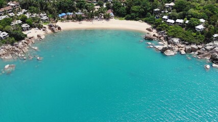 Fototapeta na wymiar Small houses on tropical island. Tiny cozy bungalows located on shore of Koh Samui Island near calm sea on sunny day in Thailand. Volcanic rocks and cliffs drone top view.