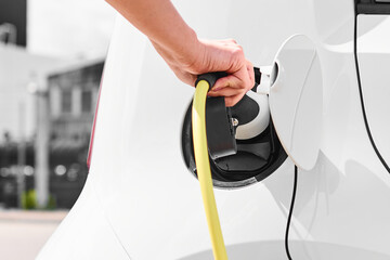 Woman plugging in electric car at electric charging station outdoors with building on the...