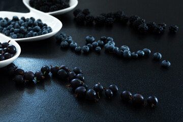 Set of different types of black berries in a white plate on a black table. Stylish seasonal vitamins