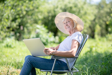 Elderly woman sitting in the deck chair with the computer