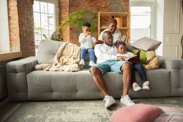 Reading. Young and cheerful african family during quarantine, insulation spending time together at home. Time for family, happiness and love. Concept of quarantine lifestyle, togetherness, home