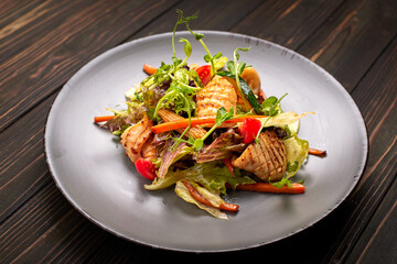Seafood salad with grilled squid, corn, carrots, tomatoes and lettuce, on a gray plate, on a wooden background © pobaralia