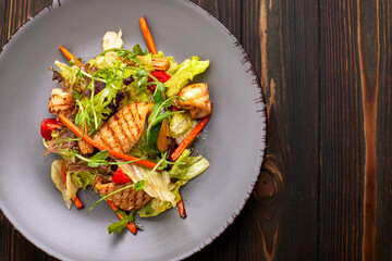 Seafood salad with grilled squid, corn, carrots, tomatoes and lettuce, on a gray plate, on a wooden background © pobaralia
