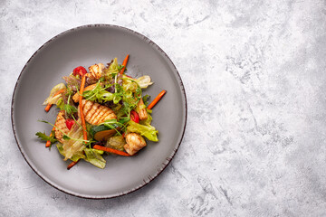 Seafood salad with grilled squid, corn, carrots, tomatoes and lettuce, on a gray plate, on a light background © pobaralia