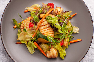 Seafood salad with grilled squid, corn, carrots, tomatoes and lettuce, on a gray plate, on a light background © pobaralia