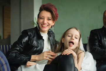 Crazy mother in black leather jaket and pants hugging her little daughter in white dress, they are...