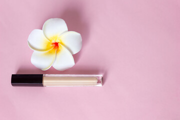 Concealer makeup corrector and flower on pink background, selective focus