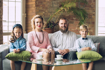 Memory. Happy family traditional portrait, old-fashioned. Cheerful parents and kids in official styled attire on dark vintage background. Concept of human emotions, memories, togetherness, fun.