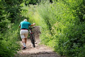 Man with bicycle going up the path in mountain forest. Summer cycling and travel on a nature