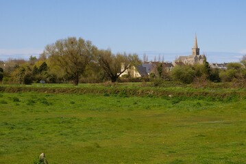 A view of a French village with church steeple across a green field in rural Normandy, France.