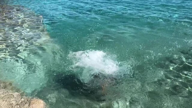 Brave young woman jumping off a cliff into the clear sea bay close-up