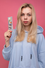 A young blogger girl holds wads of money on a pink background