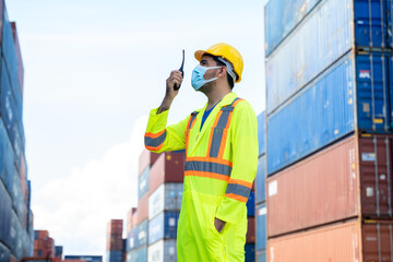 Foreman worker wearing protective mask to Protect Against Covid-19 holding radio walkie-talkie to working checking at container cargo,Import and Export concept.