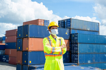 Container worker wearing protection face mask during coronavirus and flu outbreak and yellow safety hard hat helmet standing at container yard,Import and Export concept.