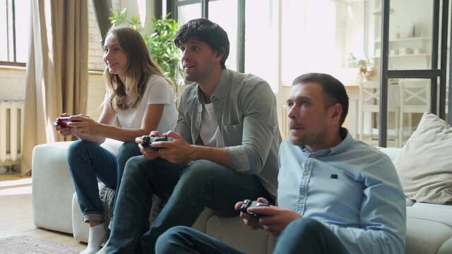 Group of young people playing games on console while having party 