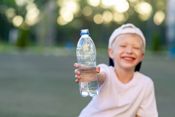 a boy sits on a green lawn on a football field and holds a bottle of water. Focus on the water bottle