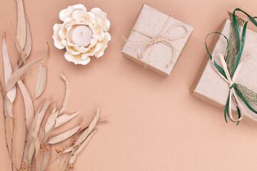 Autumn composition. Gifts wrapped in kraft paper, autumn eucalyptus leaves, candle in the shape of a flower on a beige background. Flat lay, top view, copy space