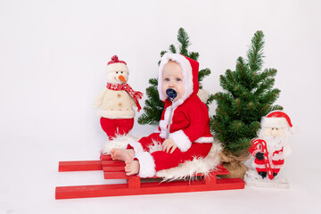 a small child is sitting in Santa's basket on a white isolated background in a hat and with Christmas trees, the concept of happy New year and Christmas, a place for text