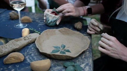 Female hands making a plate made of clay with a leaf print on it. Pottery concept.