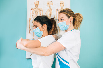 Female Caucasian physical therapy professional in a clinic doing an observation on the arm and shoulder before treating a client with a face mask