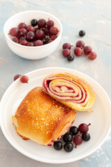 Fresh buns with berry filling decorated with black currants and gooseberry on a light blue concrete background. Vertical photo.