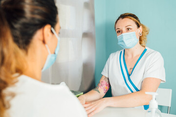 Female Caucasian physical therapy professional at a clinic explaining the treatment to be followed to a client with a face mask