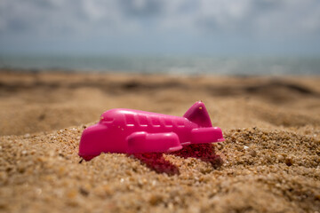 Closeup of a toy pink airplane for a sandbox lies on the sand of a sea beach. Traveling abroad concept.