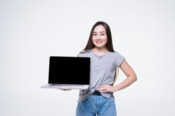 Fototapeta premium Portrait of a cheerful young asian girl pointing finger at blank screen laptop computer isolated over white background