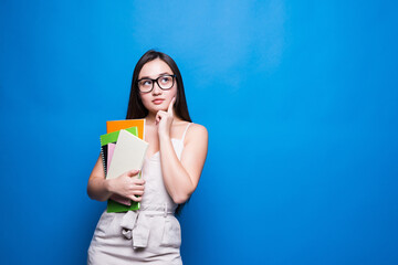 Young asian woman smiles and holds books in her hands on a blue background. Concept of education, college, session, exam.