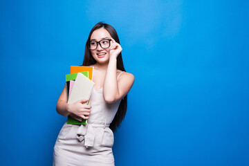 Young asian woman smiles and holds books in her hands on a blue background. Concept of education, college, session, exam.