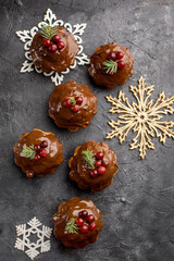 Christmas chocolate cupcakes, with icing, are decorated with a sprig of spruce, and cranberries. On a dark table dessert, with cinnamon sticks, snowflakes, serpentine. Holidays content
