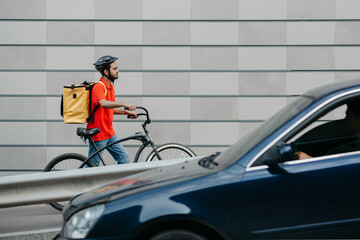 Delivery by courier in city. Guy in helmet and with backpack, going through city with bicycle