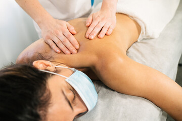 Caucasian woman receiving a physiotherapeutic shoulder massage while lying on a stretcher with a face mask