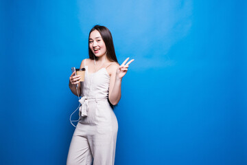 Young asian woman holding coffee cup with peace gesture isolated on blue background