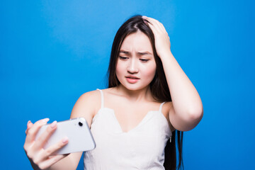 Sad gloomy asian woman using phone isolated on a blue background